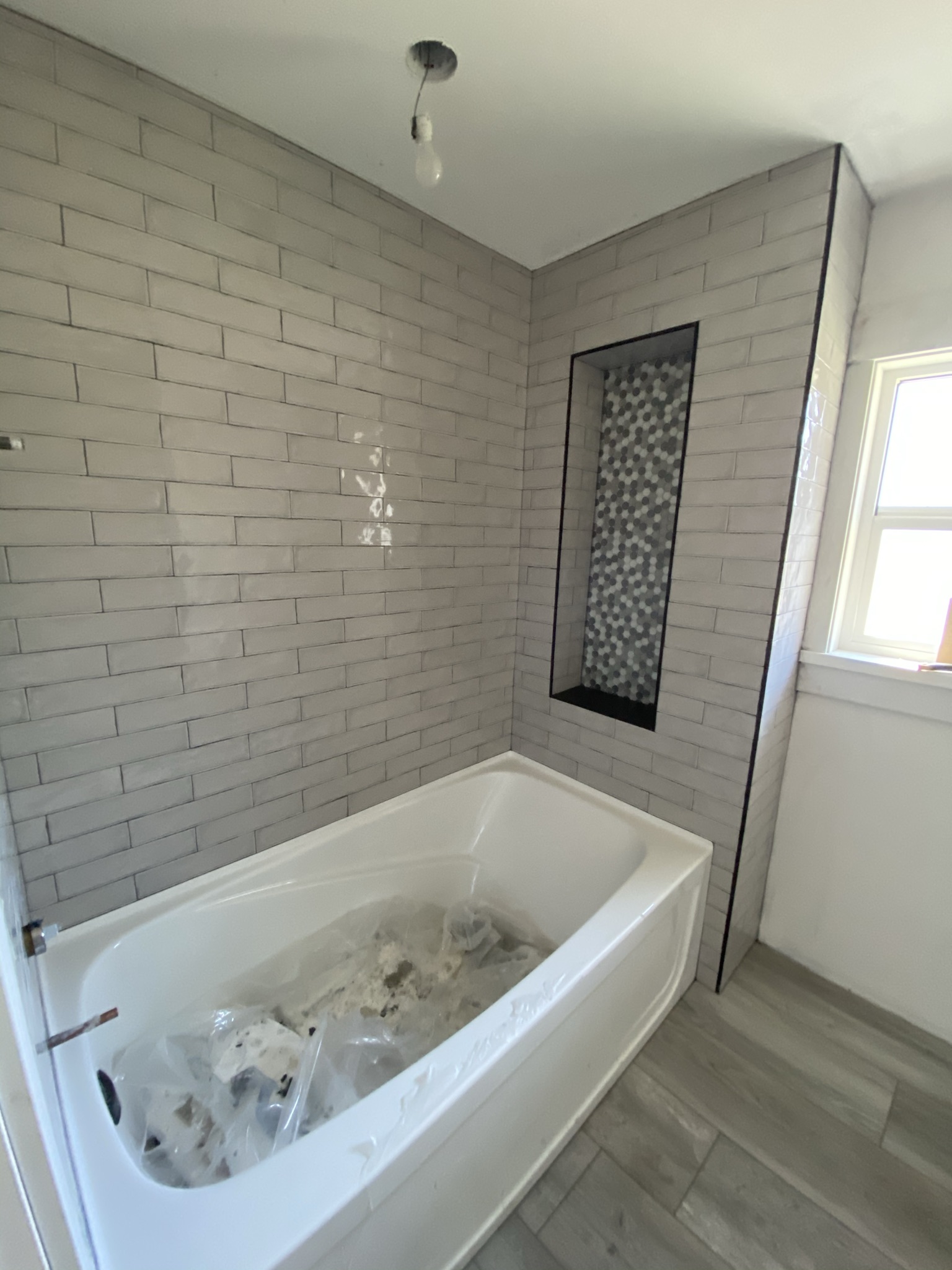 Subway tile bathroom with hex niche and wood look floor